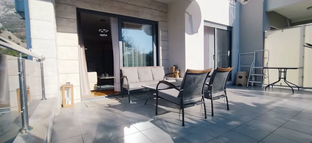Große Terrasse mit Gartenmöbeln in einer Wohnung in Bečići, Montenegro: geflieste Böden, Bergblick und Panoramafenster.