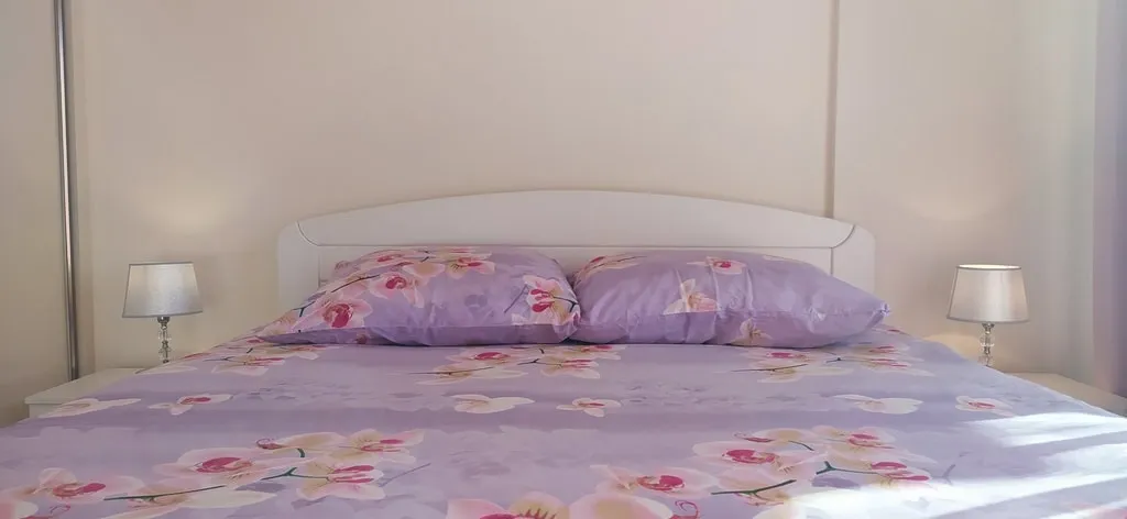 Gemütliches Schlafzimmer mit Doppelbett in einer Wohnung in Bečići, Montenegro: helles Interieur und Nachttischlampen.