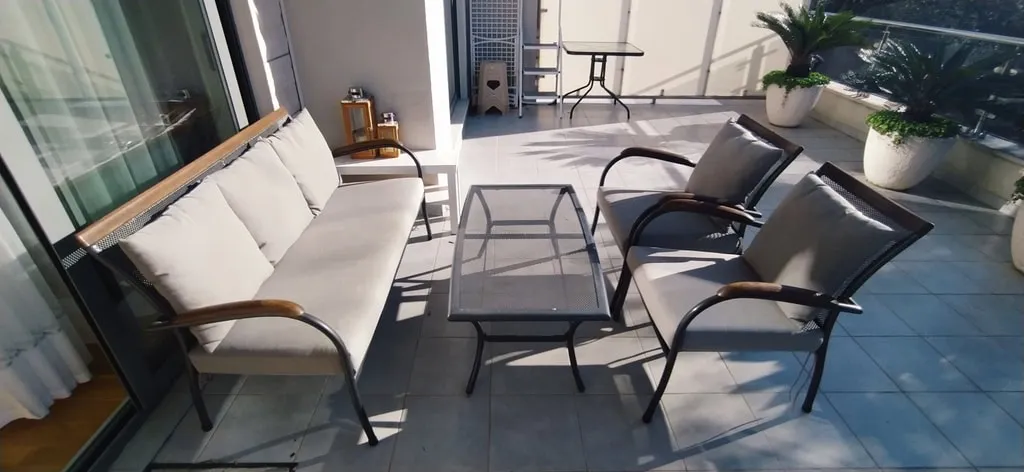 Gemütliche Terrasse mit Gartenmöbeln in einer Wohnung in Bečići, Montenegro: Sofa, Sessel und Tisch auf dem sonnigen Balkon.