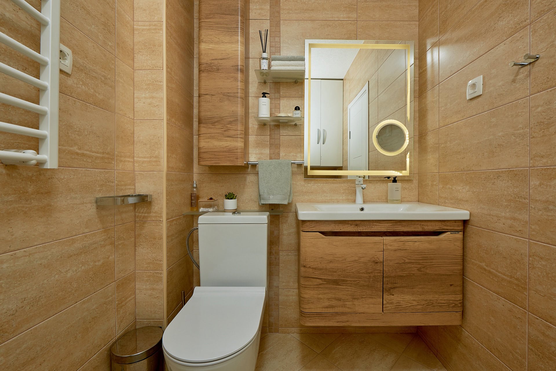Modernes Badezimmer mit weißer Sanitärkeramik, Holzunterschrank und beleuchtetem Spiegel in einer Wohnung in Bečići, Montenegro