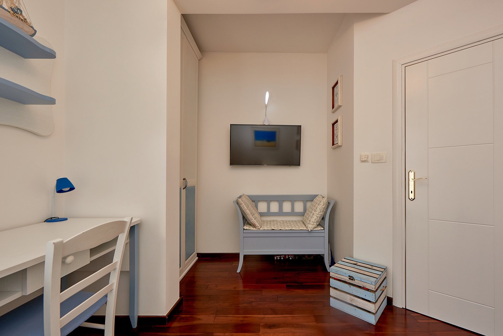 Schlafzimmerinterieur in einer Wohnung in Bečići, Montenegro: Schreibtisch, blaue Bank, Fernseher und Parkettboden.