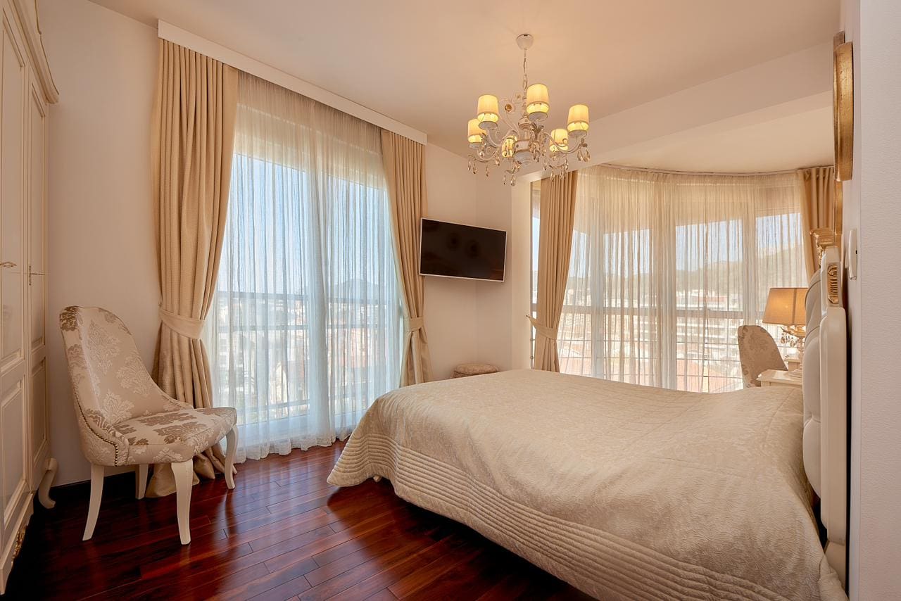 Helle Schlafzimmer mit Panoramafenstern, Doppelbett und Sessel im Penthouse in Bečići, Montenegro