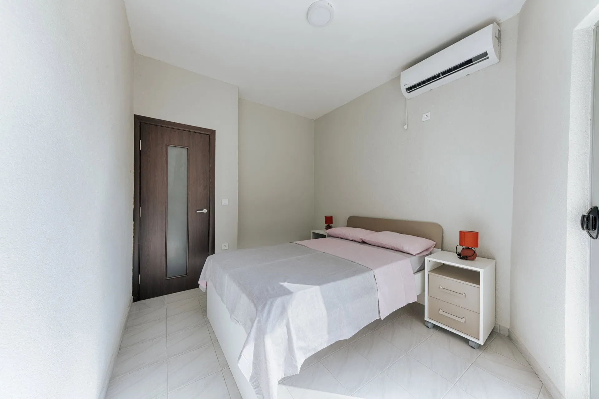 Bright bedroom with a double bed and air conditioning in a villa in Utjeha, Montenegro. Modern interior with tile flooring.