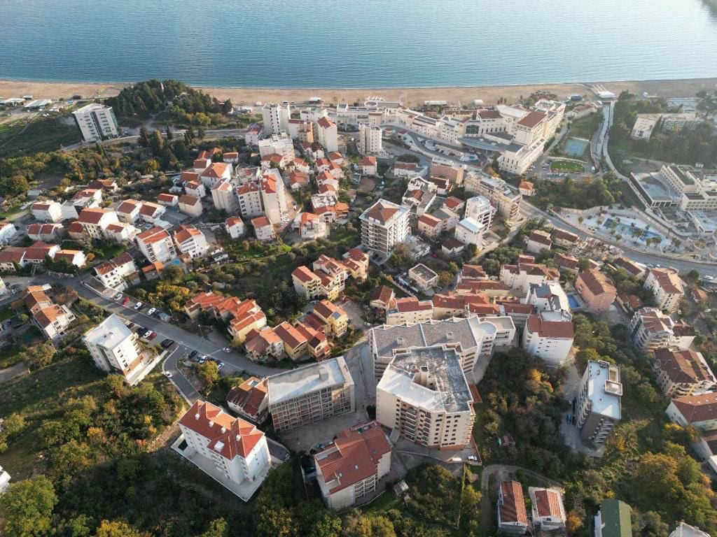 Pogled iz vazduha na stambeni kompleks i obalu u Bečićima, Crna Gora: moderne kuće sa crvenim krovovima uz more.