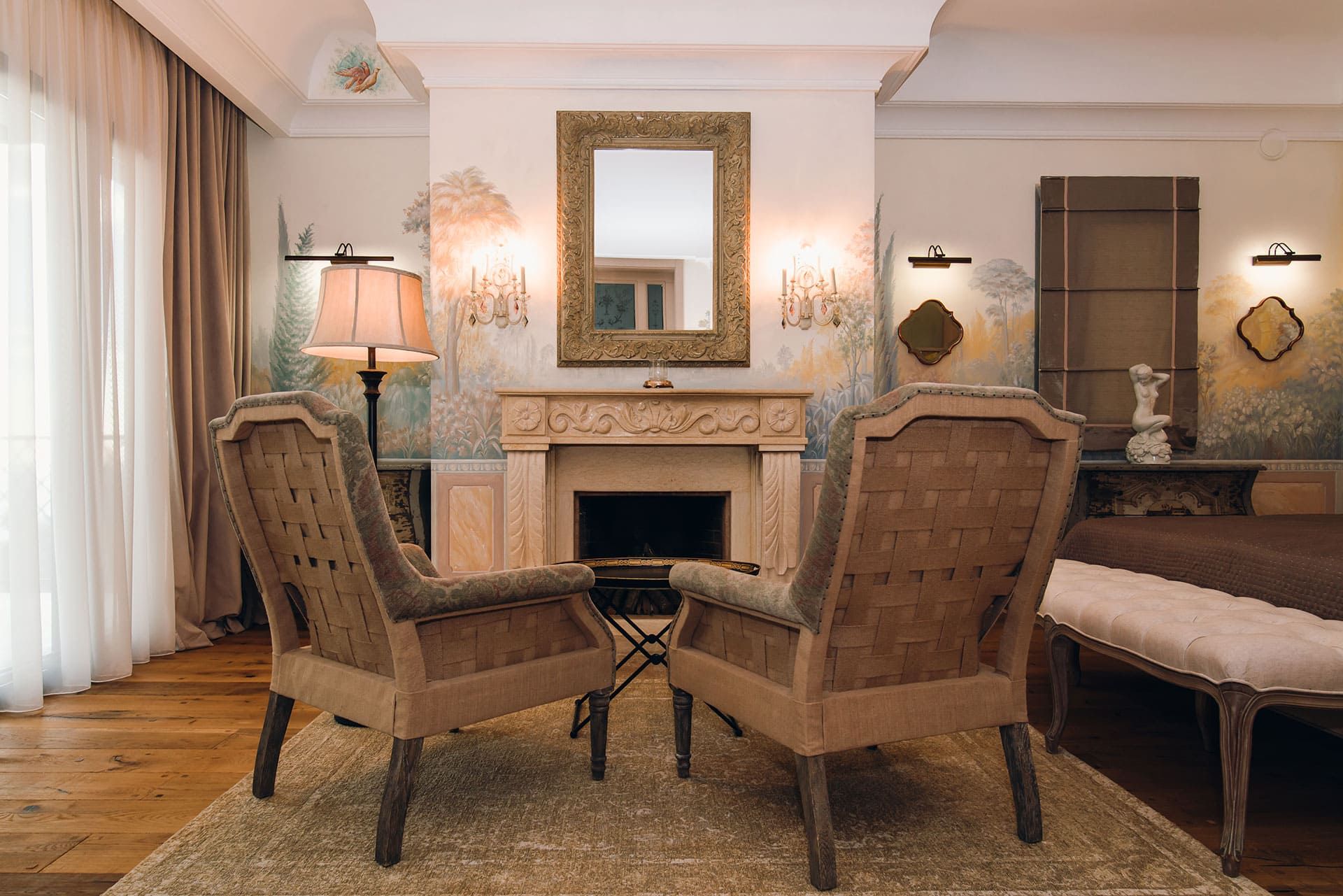 Salon de la villa à Reževići, Monténégro : cheminée, fauteuils classiques, peintures murales et miroir dans un cadre doré.