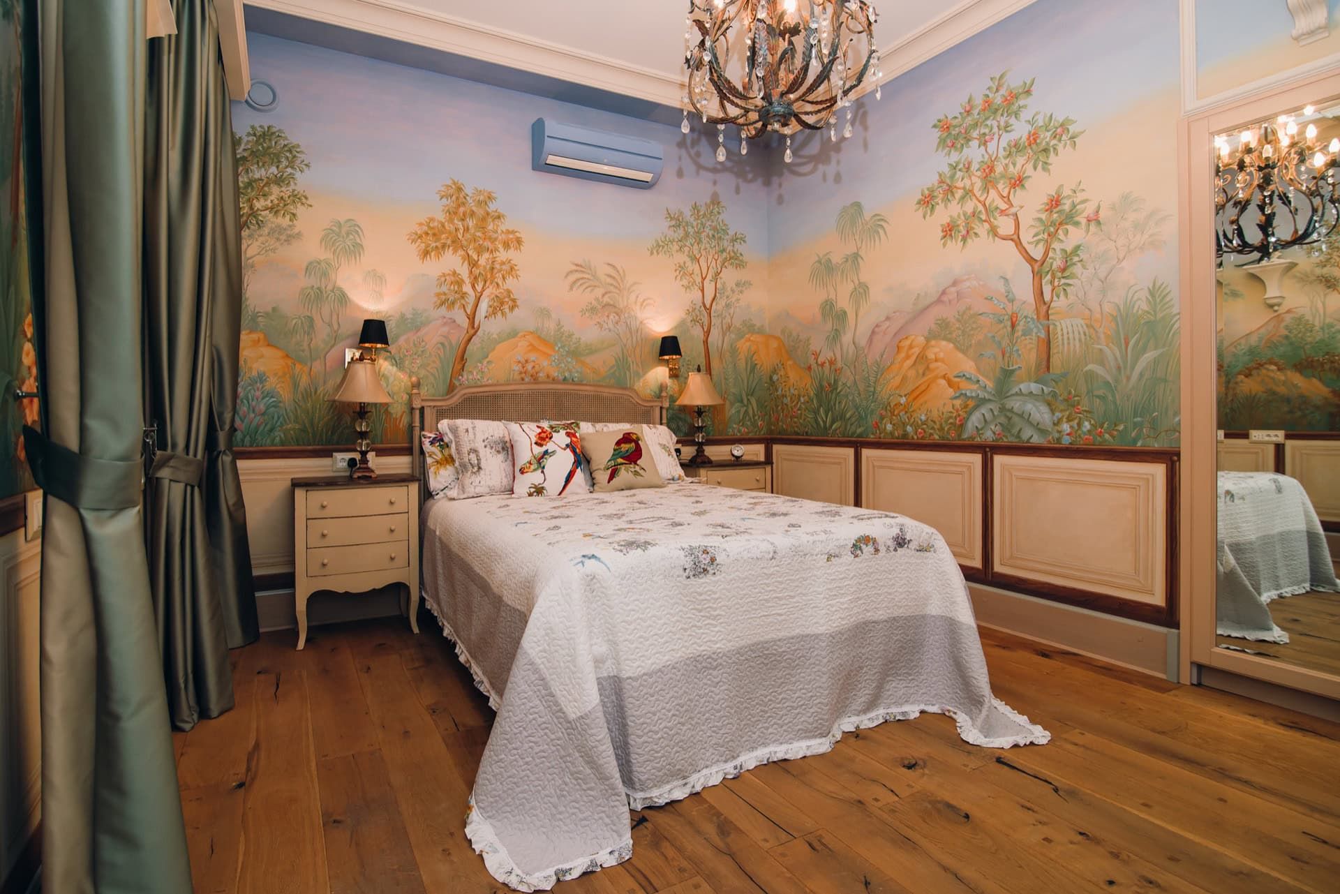 Chambre avec peinture murale, lit double et lustre dans une villa à Reževići, Monténégro. Parquet en bois, intérieur chaleureux.