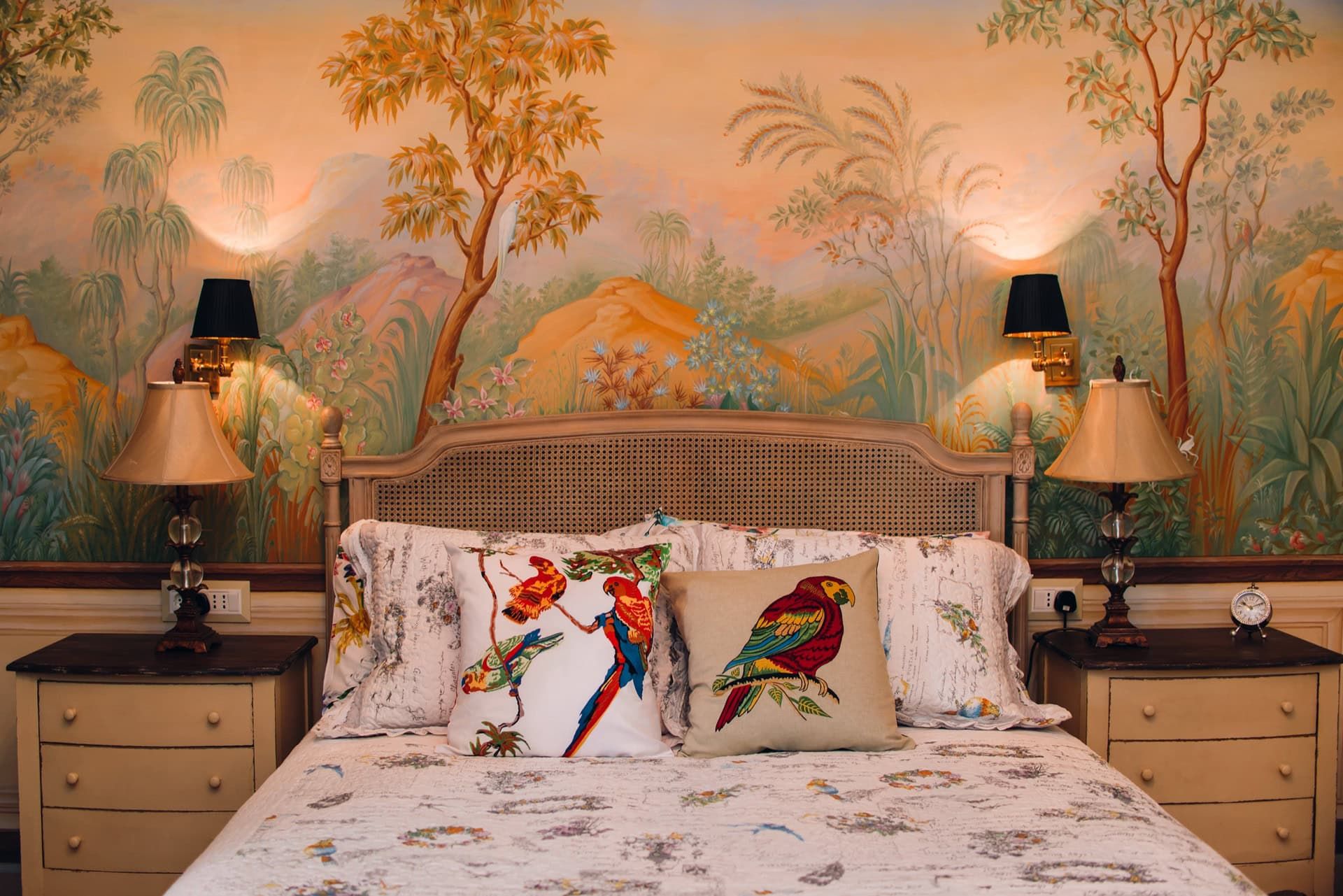 Chambre à coucher dans une villa à Reževići, Monténégro : lit avec tête de lit tressée, papier peint d’auteur avec paysage et décor avec des perroquets.