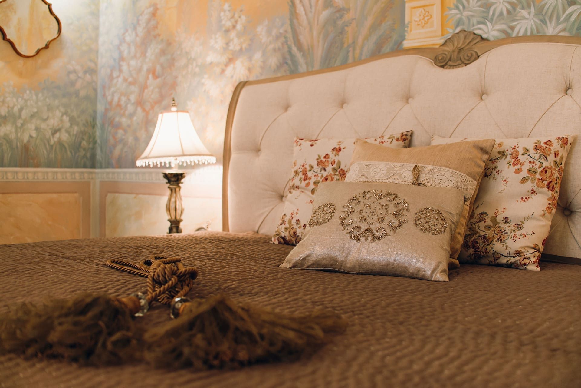 Intérieur de la chambre à coucher d’une villa à Reževići, Monténégro : lit avec tête de lit rembourrée, coussins décoratifs et peinture murale.