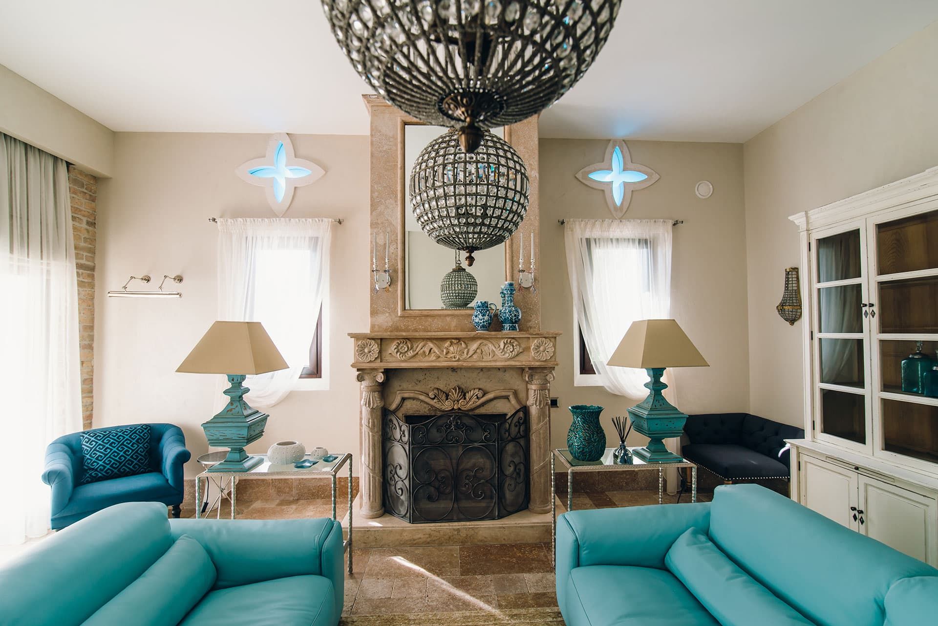 Salon luxueux avec cheminée et mobilier turquoise dans une villa à Reževići, Monténégro. Intérieur classique avec des lustres.