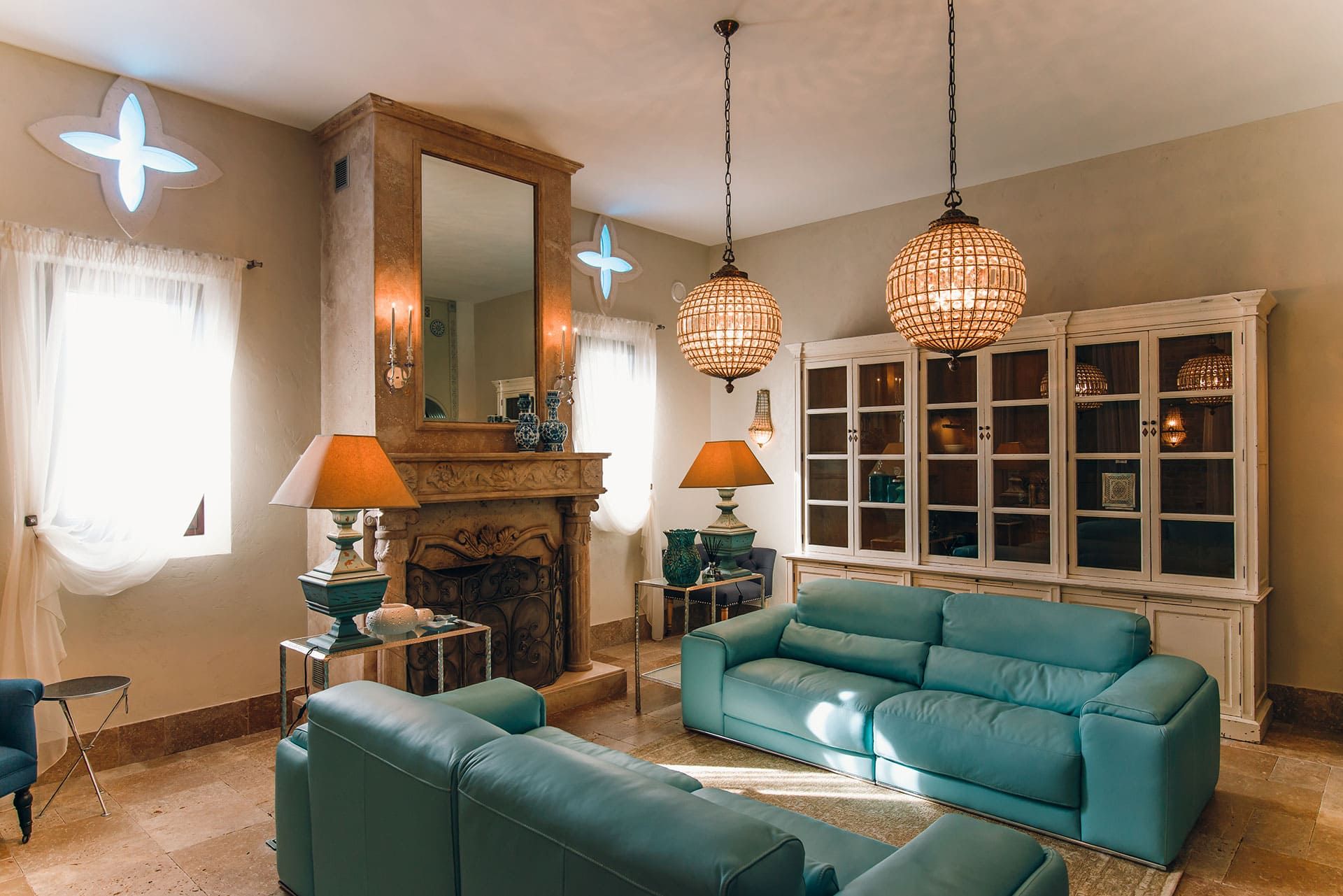 Salon de la villa à Reževići, Monténégro : canapés en cuir turquoise, cheminée en pierre, armoire vintage et lustres.