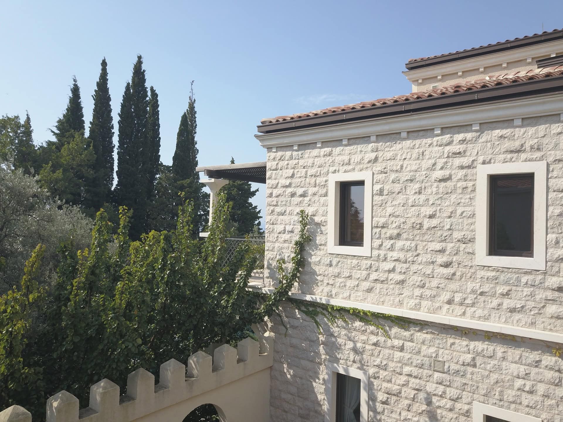 Façade d’une villa en pierre de style méditerranéen avec terrasse et cyprès, Reževići, Monténégro.