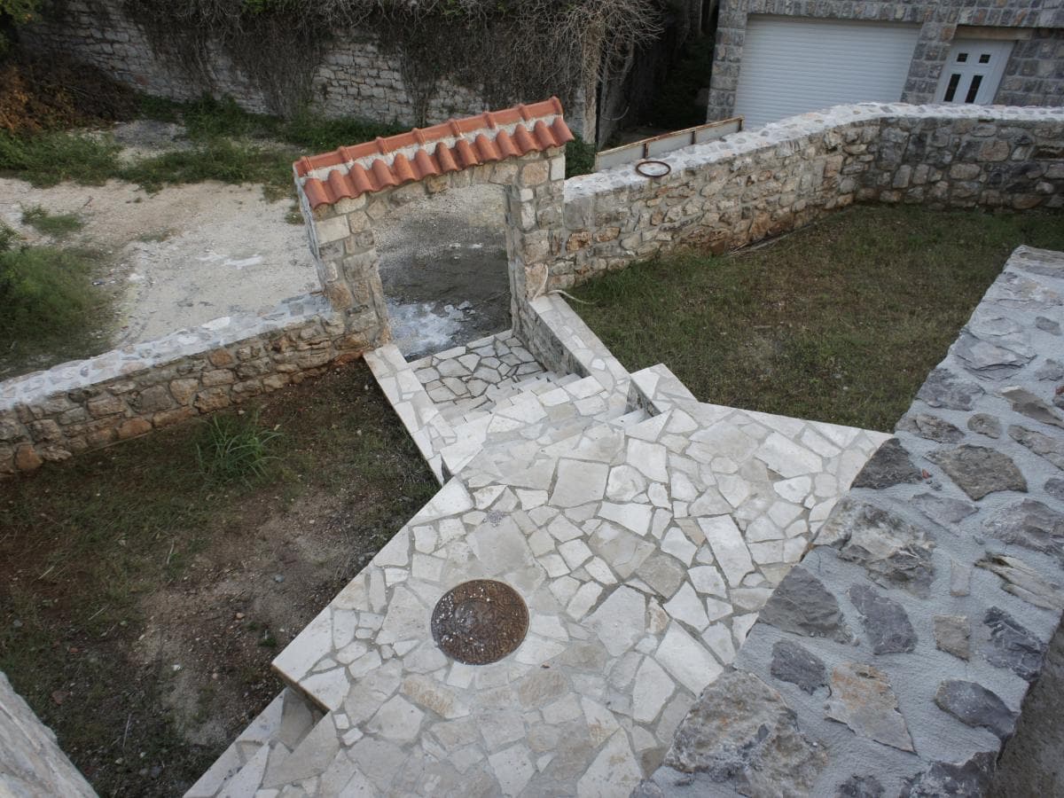 Steinerner Hof und Eingangsbereich der Wohnanlage in Radovići, Montenegro: Natursteinpflaster und Bogen.