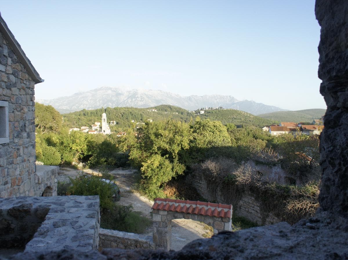 Blick aus einem Steinhaus auf die Berge und die Kirche im Ort Radovići, Montenegro: Panorama der Natur und historische Architektur.