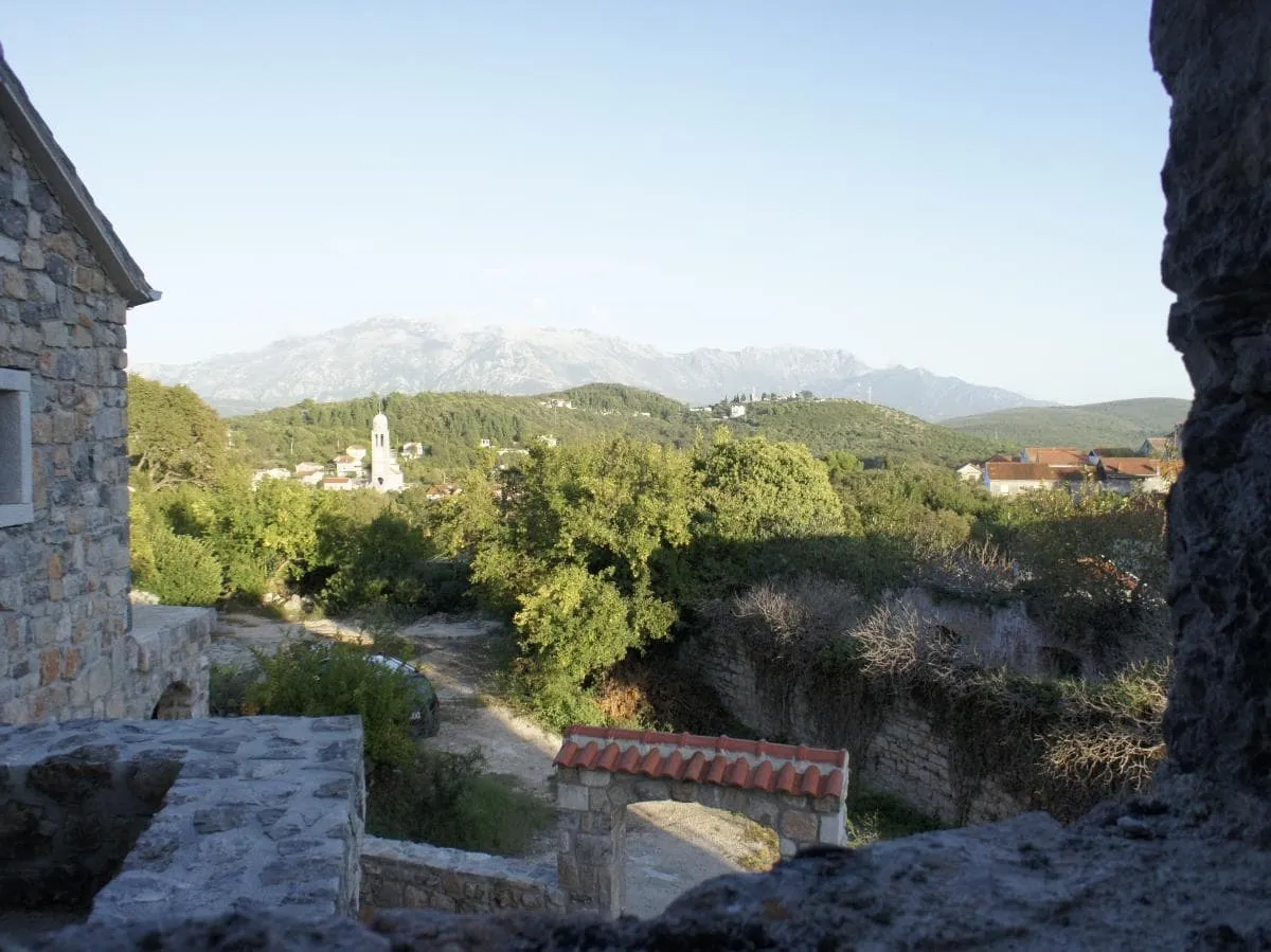 View from a stone house of the mountains and church in the village of Radovici, Montenegro: a panorama of nature and historic architecture.