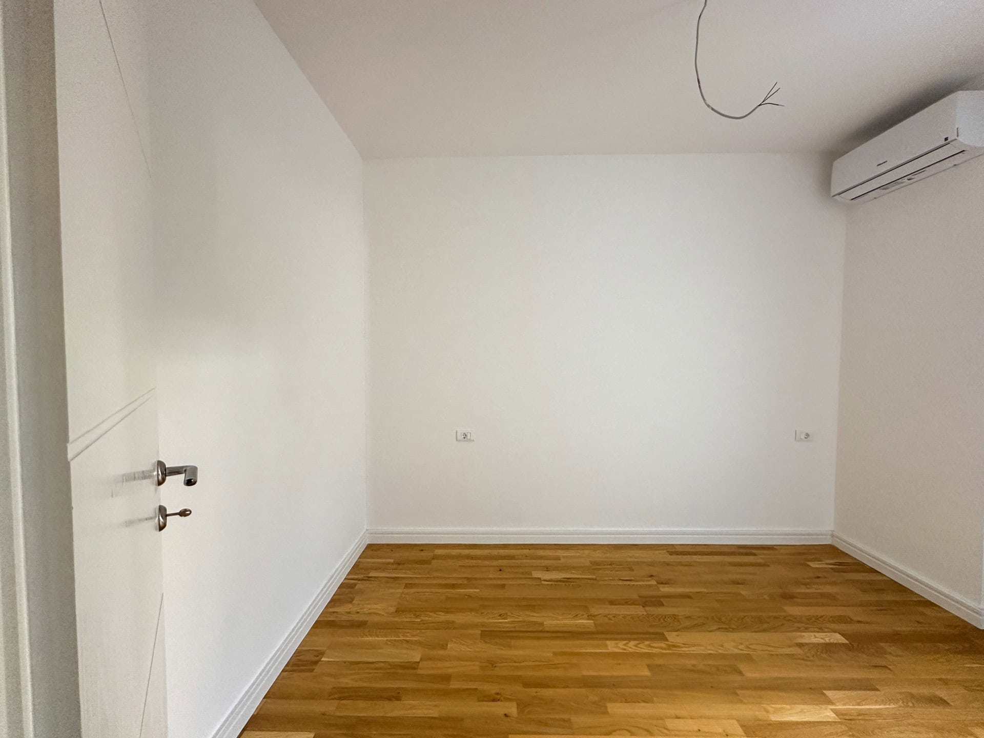 Helles Schlafzimmer mit Parkett und Klimaanlage in einer neuen Wohnung in Bečići, Montenegro. Leerer Raum mit weißen Wänden.