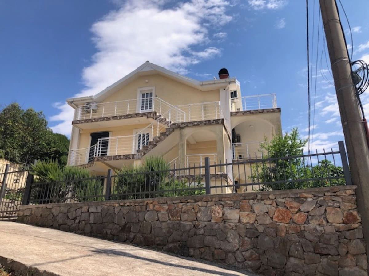 Karadağ, Krimovitsa’da iki katlı villa: açık renkli cephe, korkuluklu açık teraslar ve taş çevre duvarı.
