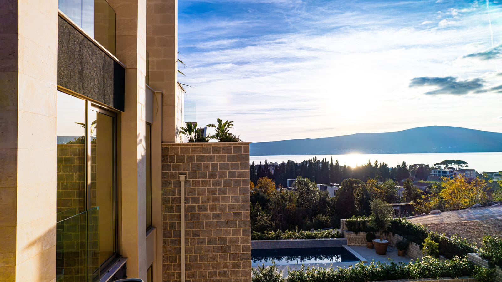 Moderne Villa in Tivat, Montenegro: Blick auf den Pool, Steinverkleidung der Fassade und Panoramablick auf das Meer und die Berge.