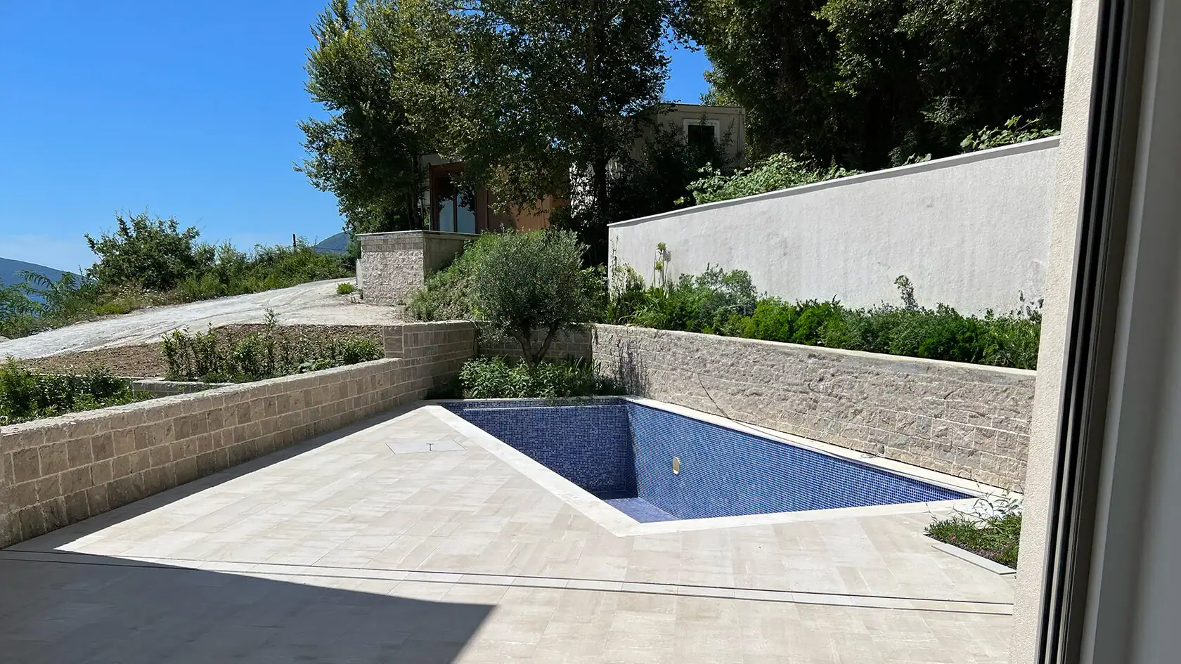 Offener Pool mit blauer Mosaikverkleidung und Steinterrasse in einer Wohnanlage in Tivat, Montenegro.
