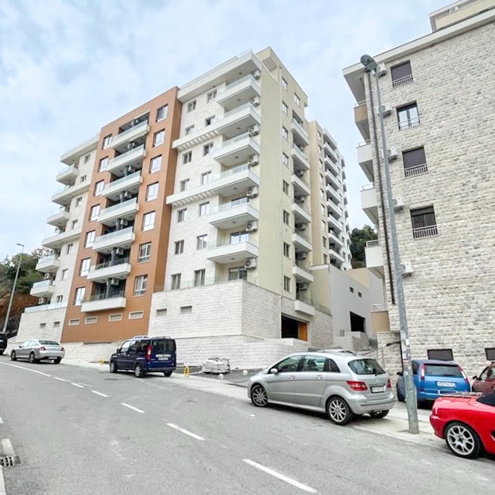 Savremeni stambeni kompleks sa balkonima u Bečićima, Crna Gora: pogled na višespratnicu sa parkingom ispred fasade.