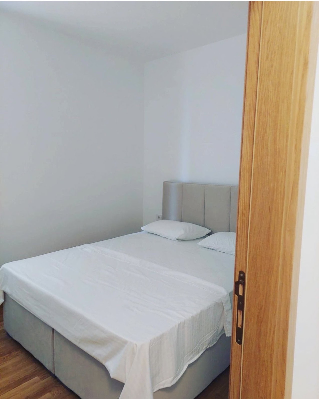 Svetla spavaća soba sa bračnim krevetom u stanu u Bečićima, Crna Gora. Moderan enterijer, drveni pod.