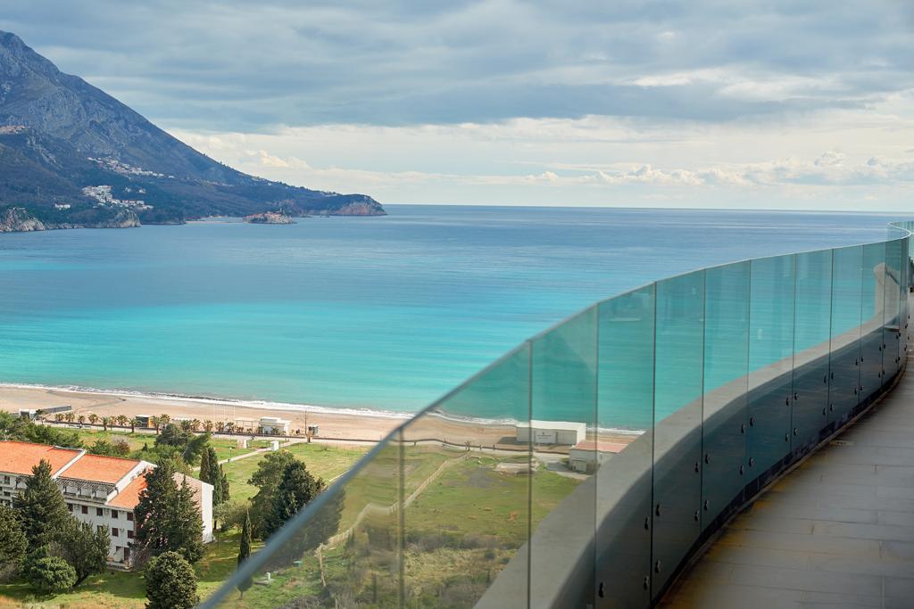 Panoramiczny widok na morze i plażę z balkonu apartamentu w Bečići, Czarnogóra, ze szklaną balustradą i tarasem.
