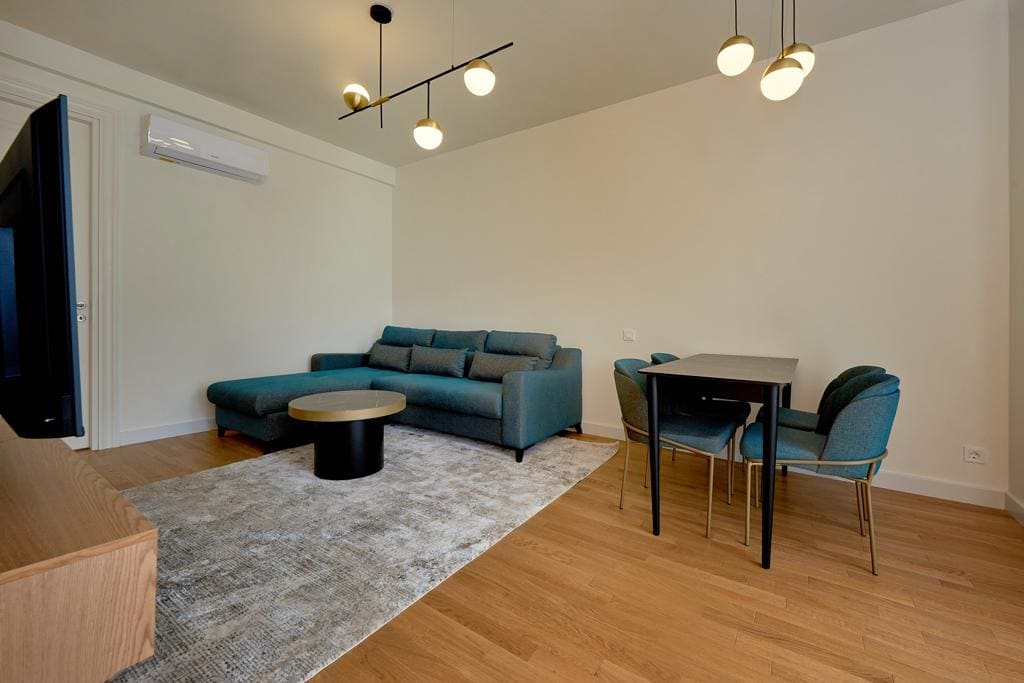 Nowoczesny salon z niebieską sofą i jadalnią w apartamencie w Bečići, Czarnogóra. Jasne wnętrze z parkietem.