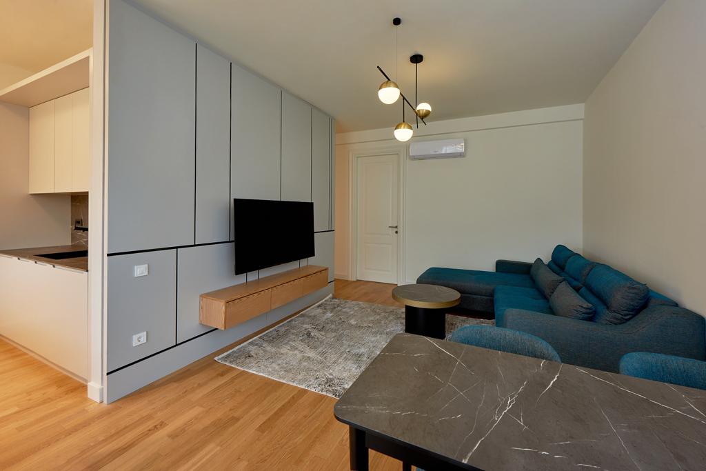 Nowoczesny salon w apartamencie w Bečići, Czarnogóra: niebieska sofa, marmurowy stolik i designerska strefa TV.