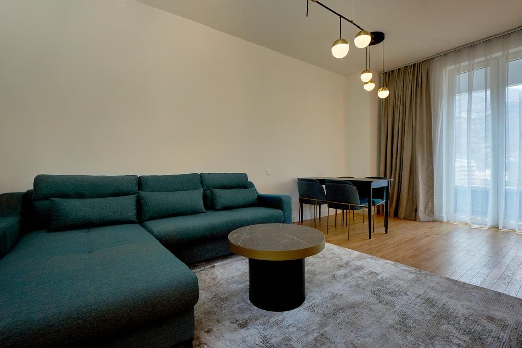 Nowoczesny salon z niebieską sofą i jadalnią w apartamencie w Bečići, Czarnogóra, z wyjściem na balkon.