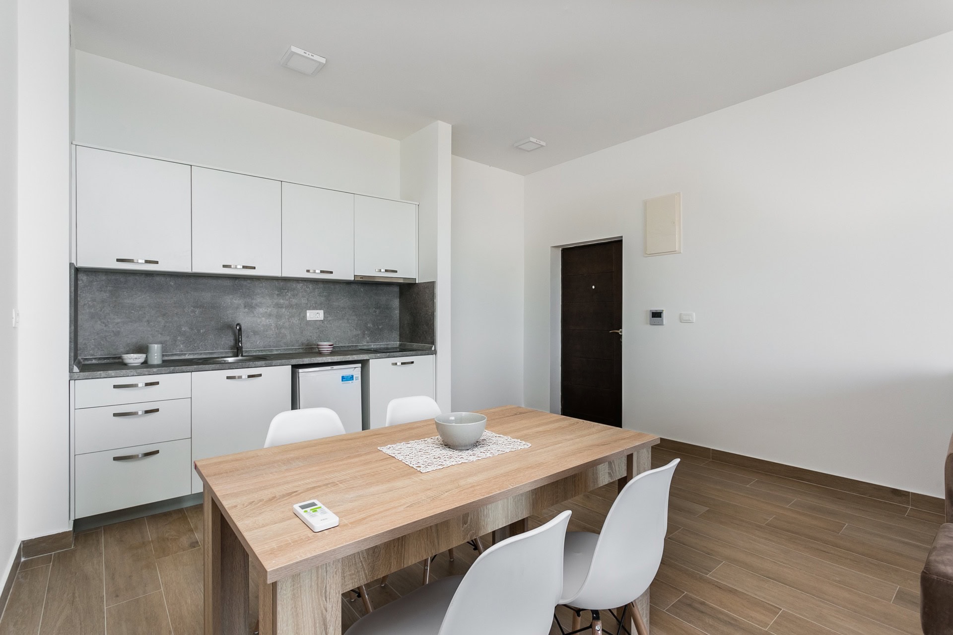 Cuisine-salle à manger moderne dans un appartement, Budva, Monténégro : façades blanches, table et chaises en bois, intérieur élégant.