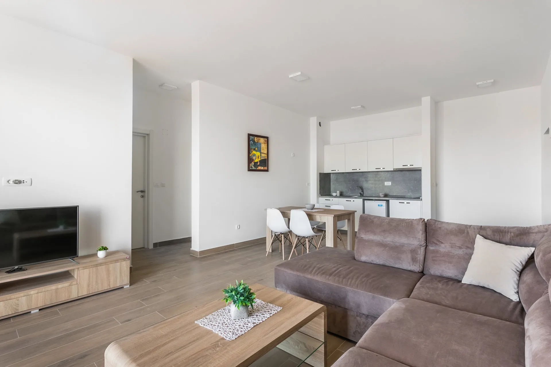 Modernes Wohnzimmer mit Küche in einer Wohnung in Budva, Montenegro: braunes Sofa, Essbereich und helle Ausstattung.