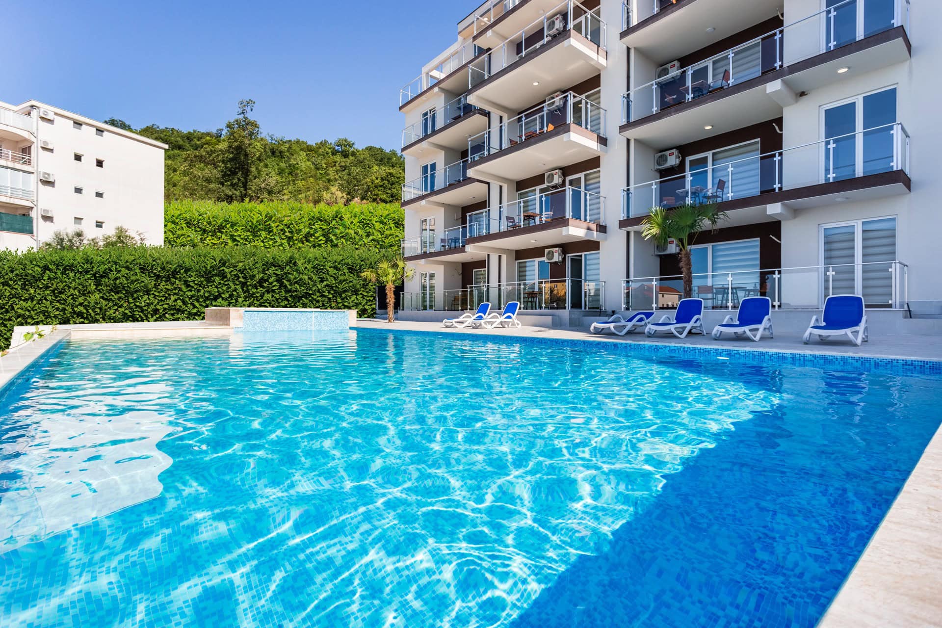 Complexe résidentiel moderne avec piscine et chaises longues à Seoce, Budva, Monténégro. Vue sur les appartements avec terrasses.