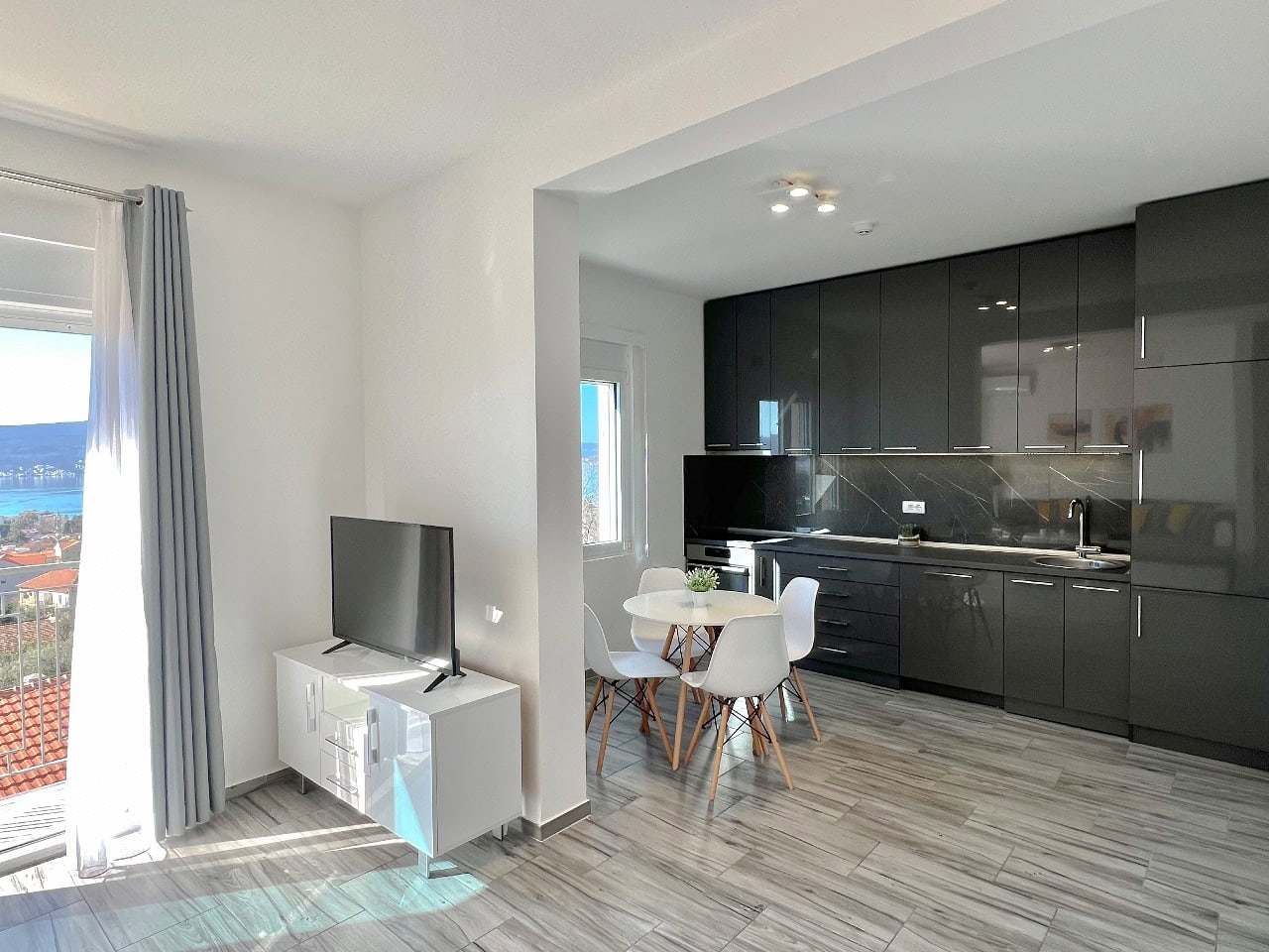 Modernes Wohnzimmer mit Küche in einer Wohnung in Tivat, Montenegro: dunkle Einbauküche, Essbereich und Meerblick.