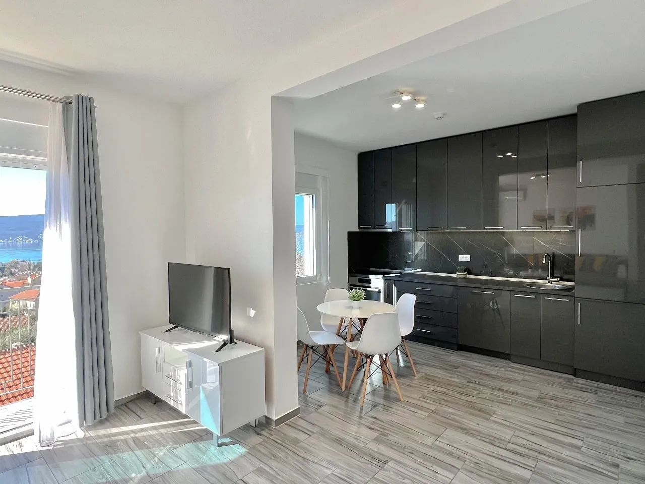 Modernes Wohnzimmer mit Küche in einer Wohnung in Tivat, Montenegro: dunkle Einbauküche, Essbereich und Meerblick.