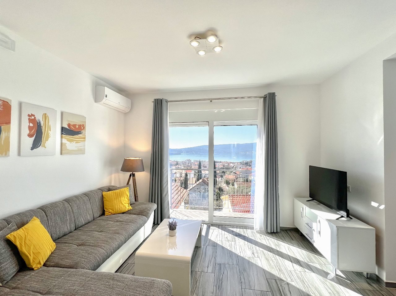 Helles Wohnzimmer in einer Wohnung in Tivat, Montenegro: graues Sofa, Meer- und Bergblick, modernes Interieur.