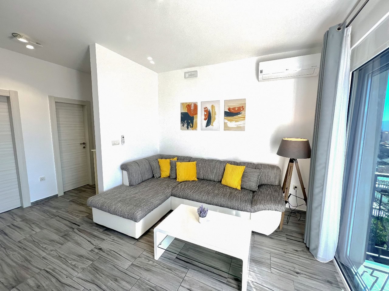 Modernes Wohnzimmer mit grauem Ecksofa und weißem Tisch in einer zum Verkauf stehenden Wohnung in Tivat, Montenegro.