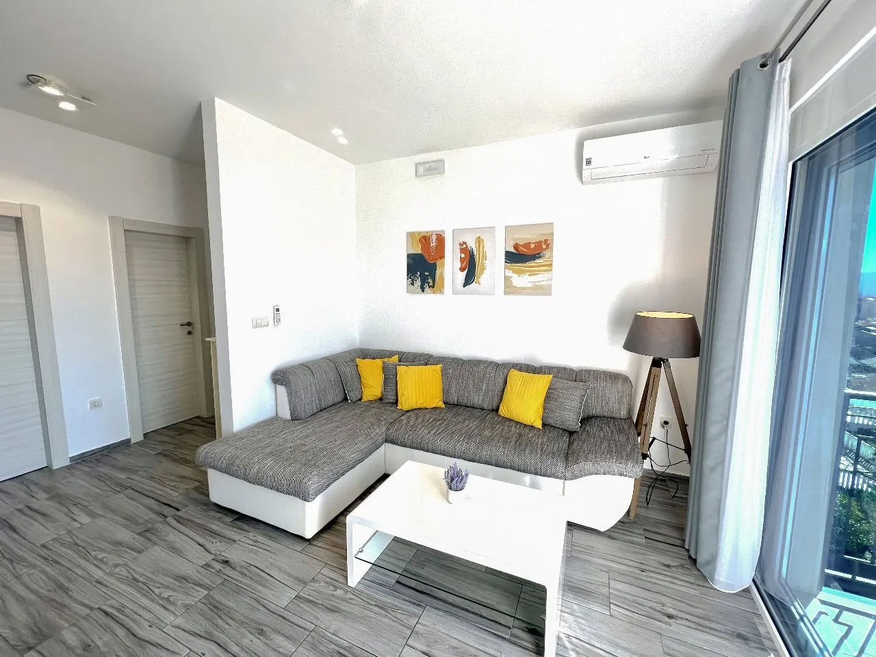 Modernes Wohnzimmer mit grauem Ecksofa und weißem Tisch in einer zum Verkauf stehenden Wohnung in Tivat, Montenegro.