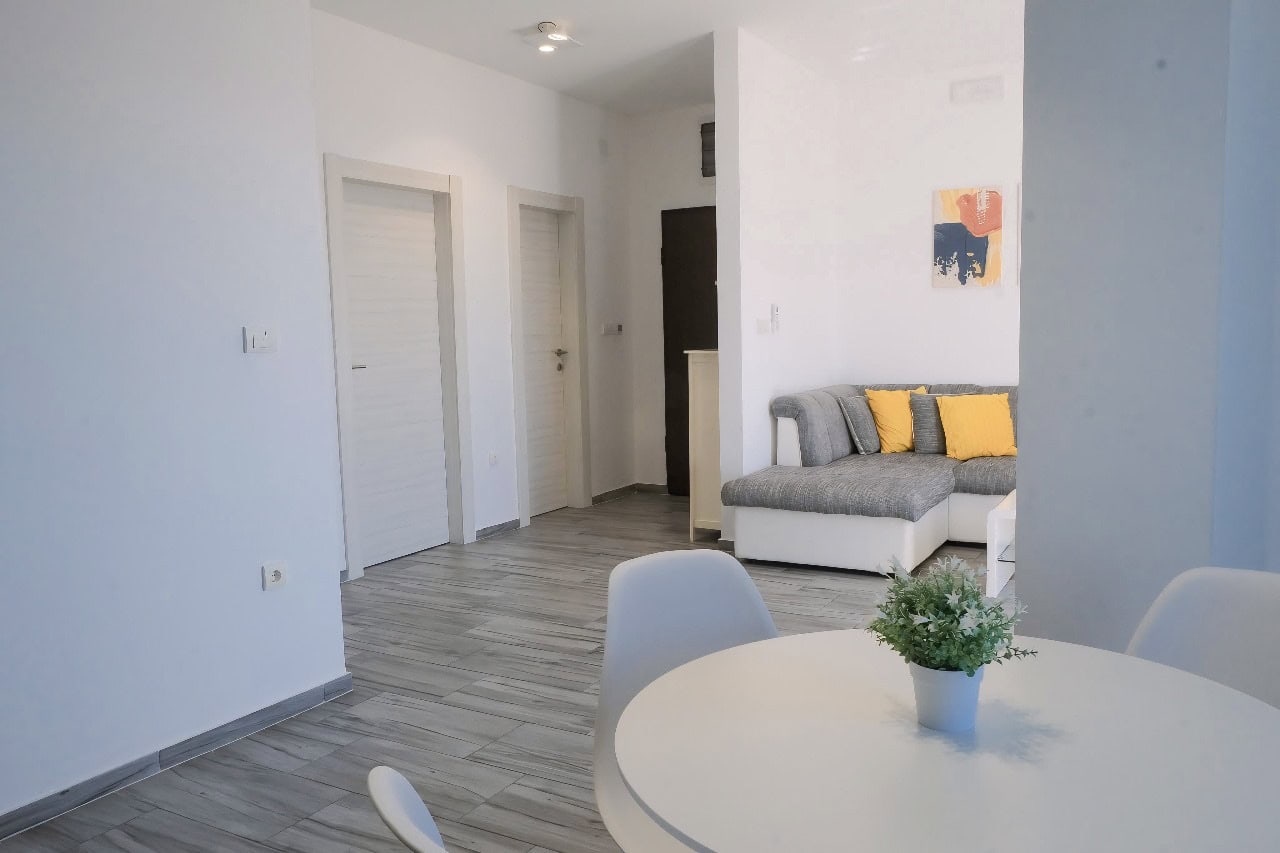 Modernes Wohnzimmer mit grauem Sofa und Essbereich in einer Wohnung in Tivat, Montenegro. Helles Interieur.