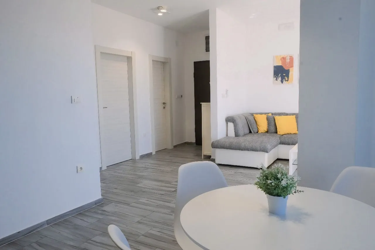Modernes Wohnzimmer mit grauem Sofa und Essbereich in einer Wohnung in Tivat, Montenegro. Helles Interieur.