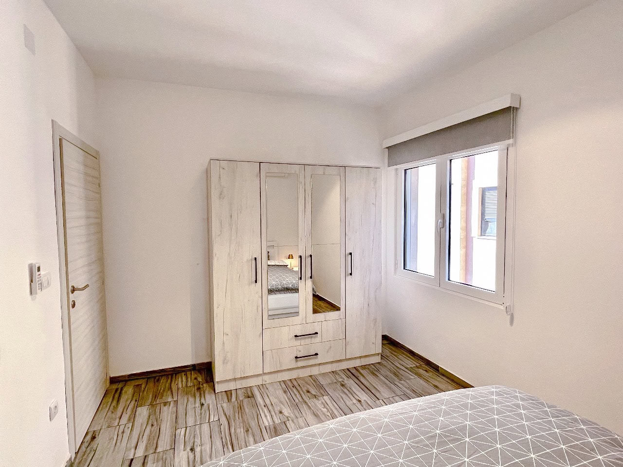 Helles Schlafzimmer in einer Wohnung in Tivat, Montenegro: Kleiderschrank mit Spiegeln, Fliesenboden in Holzoptik und modernes Interieur.