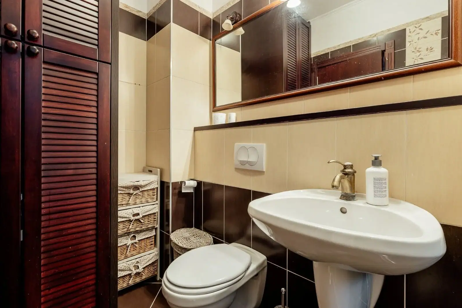 Bathroom in an apartment in Kostanica, Montenegro: brown-toned tiles, a wooden cabinet, and a mirror.