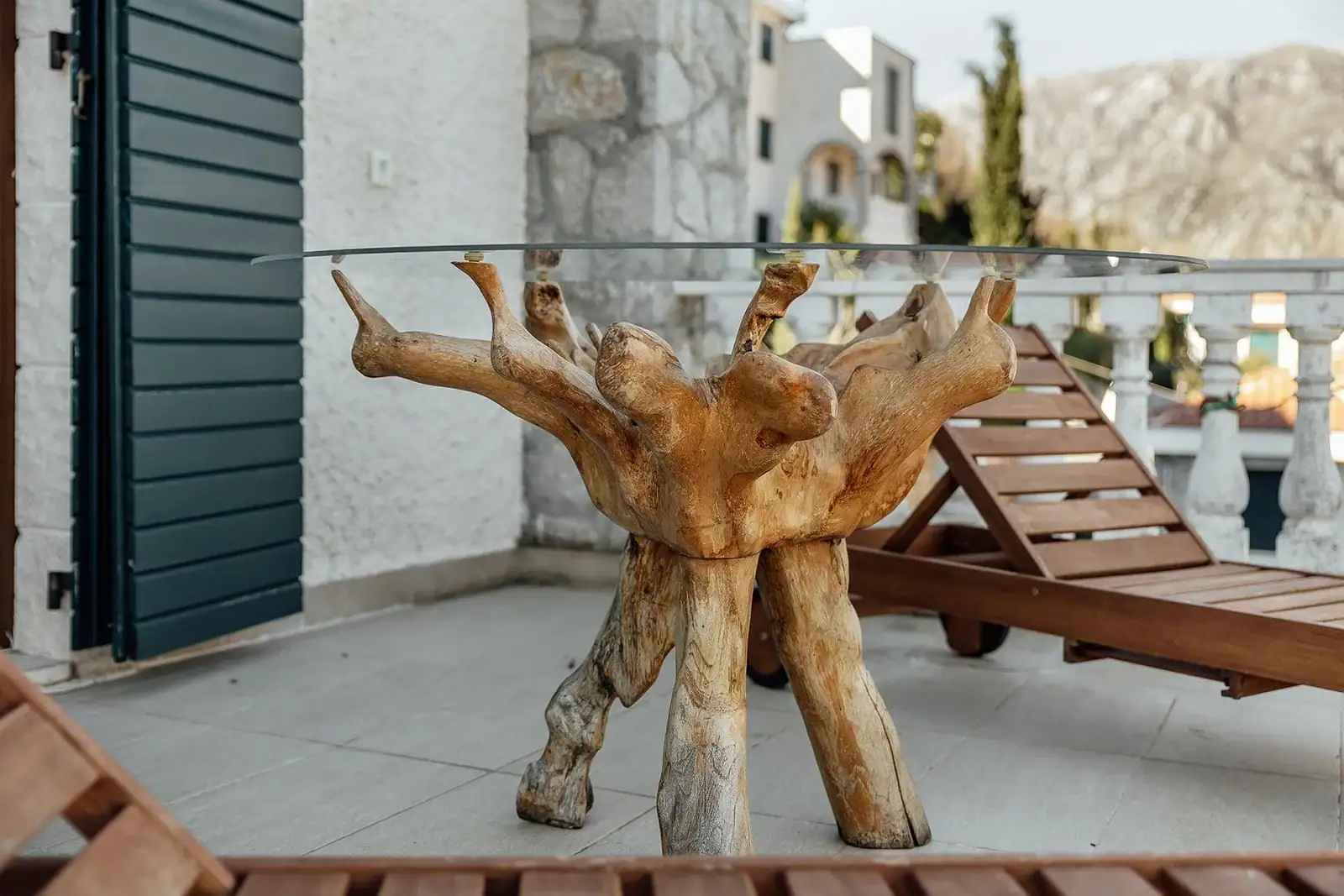 Designer table made from a tree root on the balcony of an apartment in Kostanica, Montenegro, with mountain views and lounge chairs.