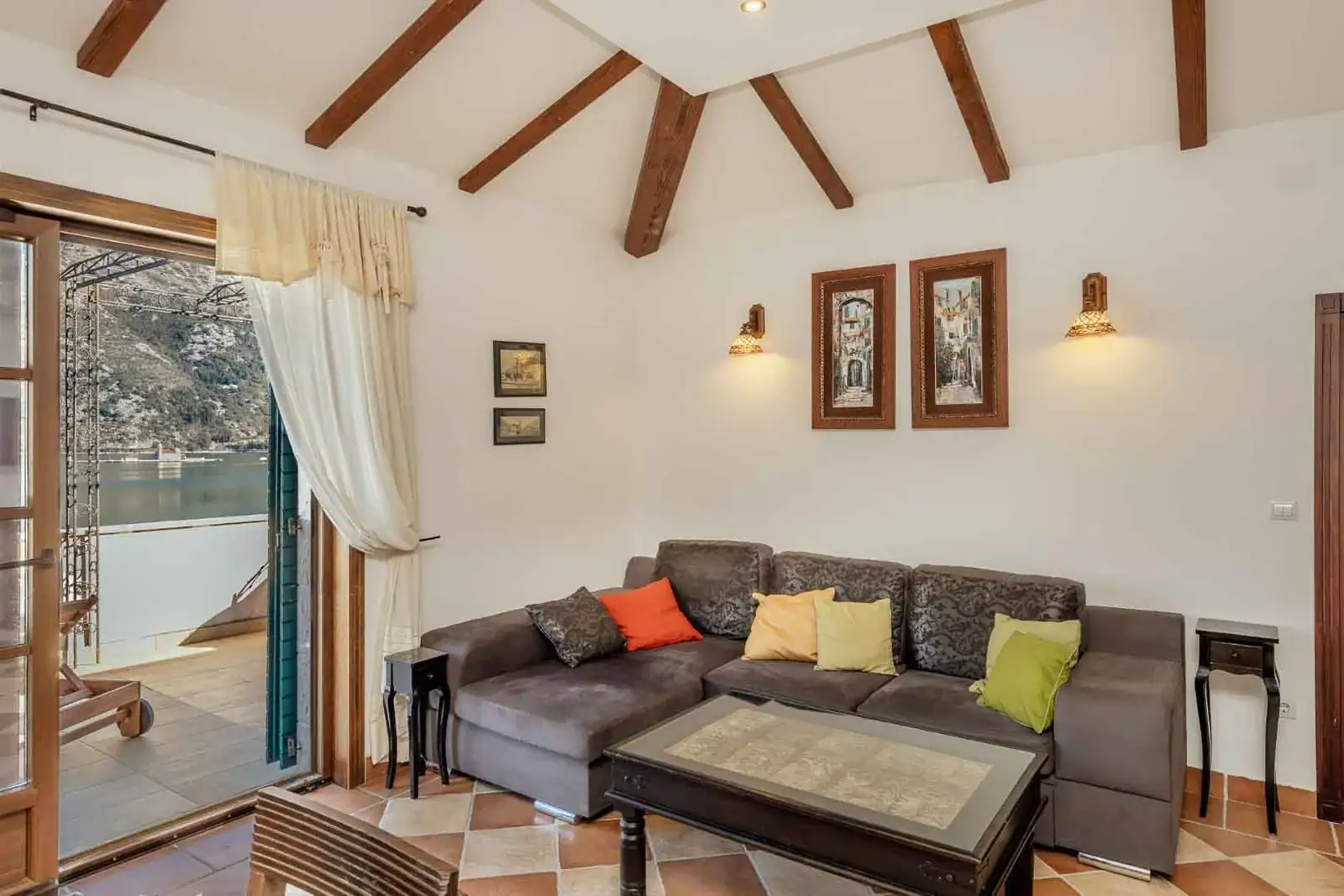 Living room with terrace and sea view in an apartment in Kostanjica, Montenegro: a soft sofa, beam ceiling, and tile flooring.