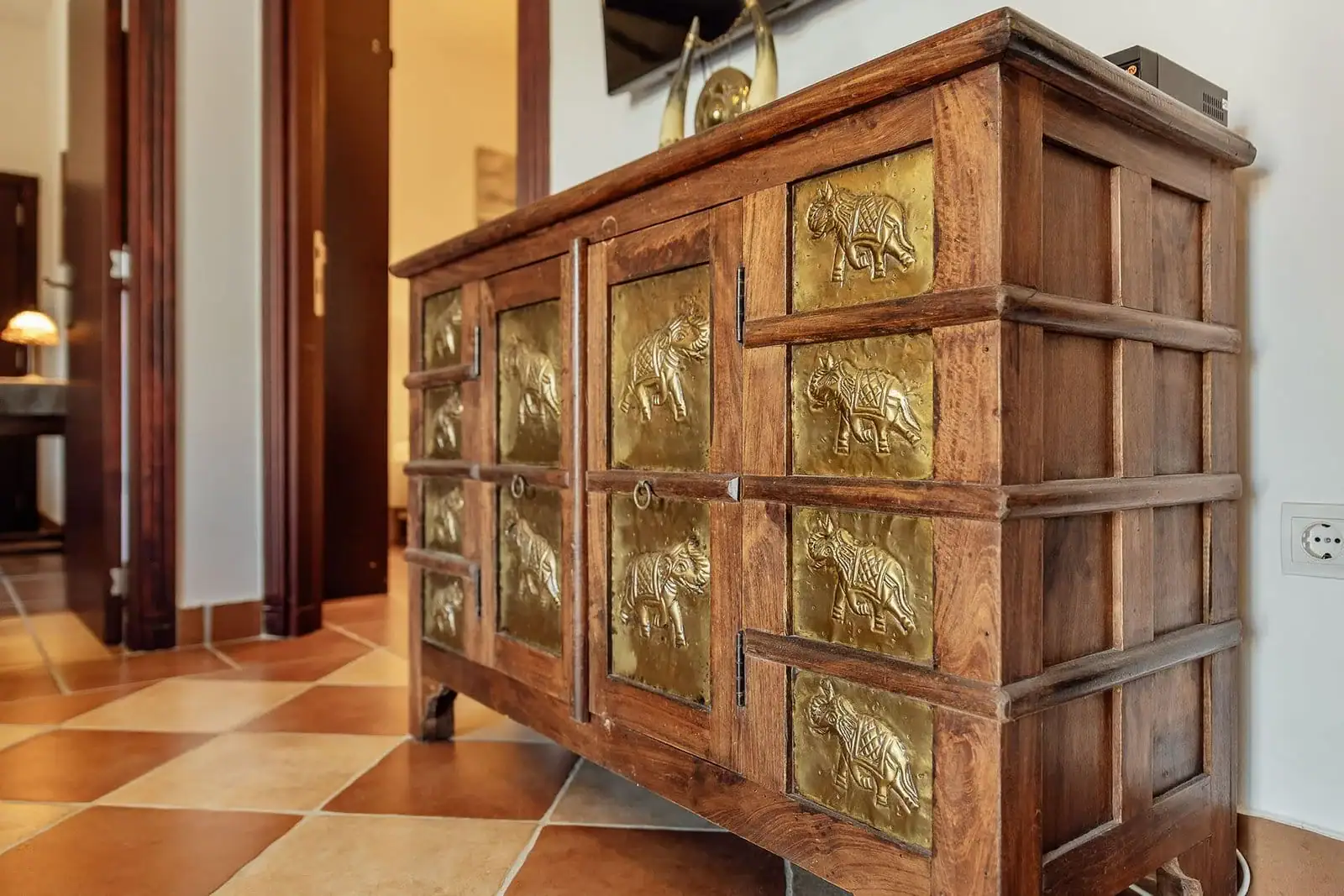 A wooden dresser with brass inlays in the interior of an apartment in Kostanica, Montenegro, against a tiled floor.