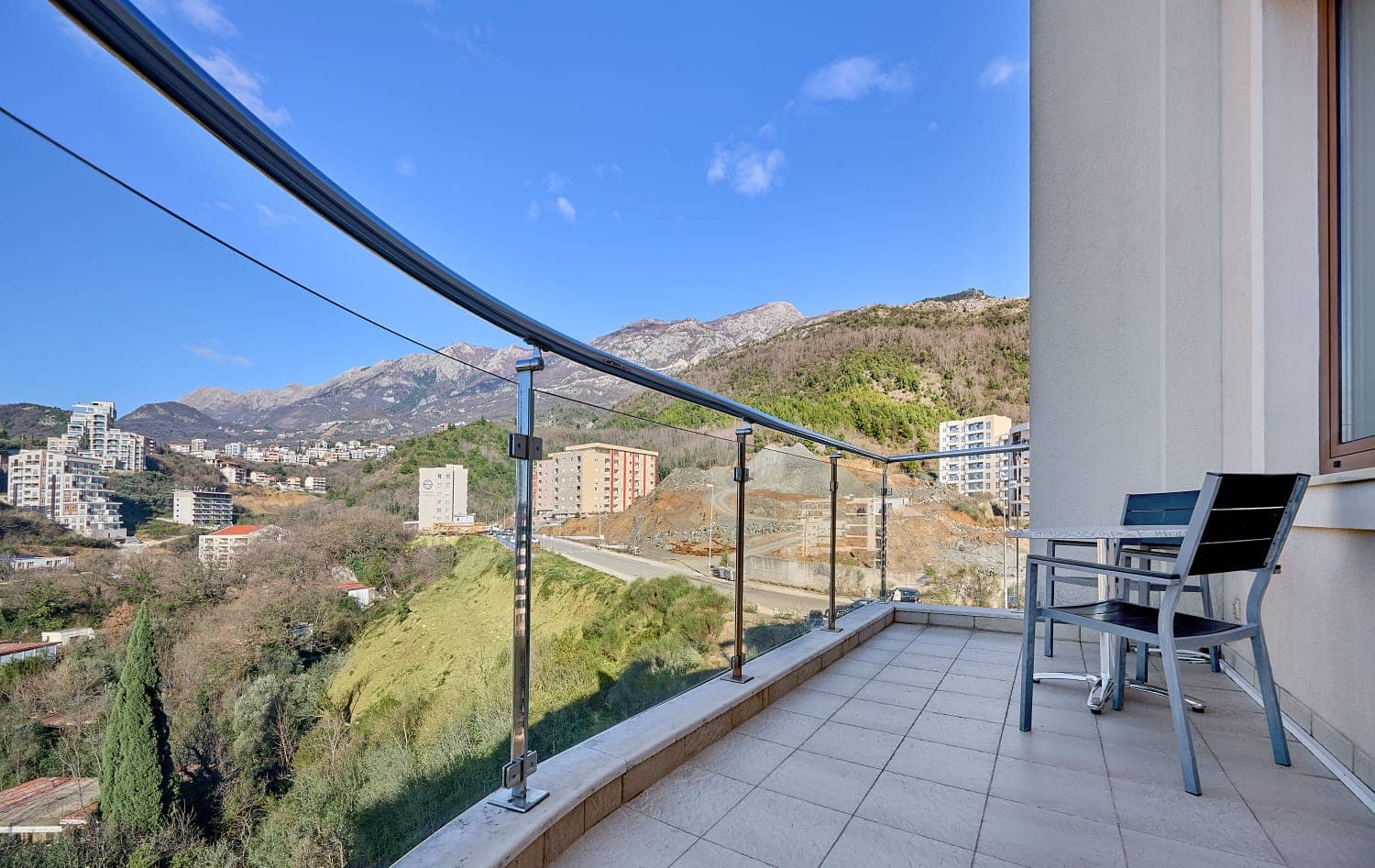 Balkon sa nameštajem i panoramskim pogledom na planine i grad Bečiće, Crna Gora. Moderna ograda od stakla i metala.