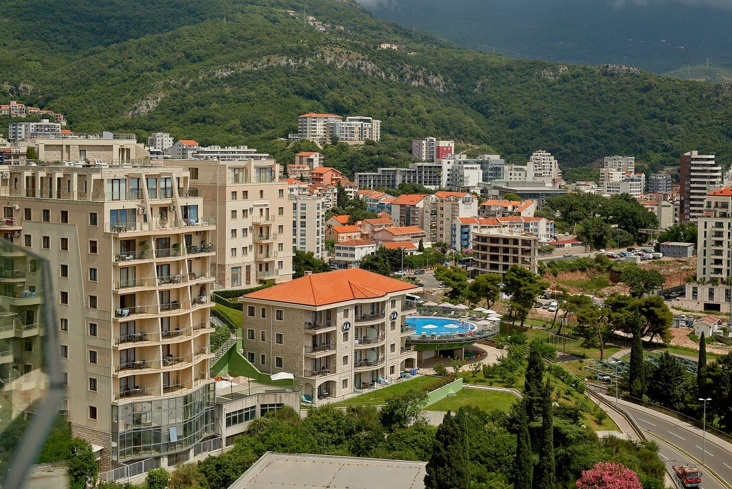 Panoramski pogled na stambeni kompleks sa bazenom i planine u Bečićima, Crna Gora: moderne kuće i gradska infrastruktura.