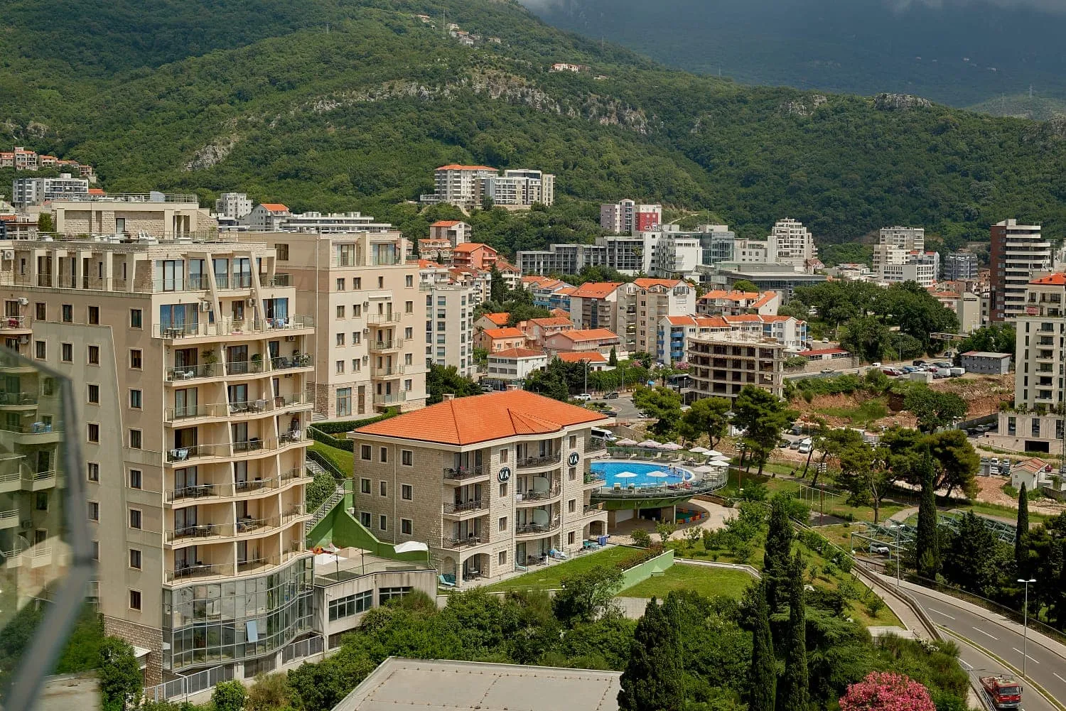 Panoramski pogled na stambeni kompleks sa bazenom i planine u Bečićima, Crna Gora: moderne kuće i gradska infrastruktura.