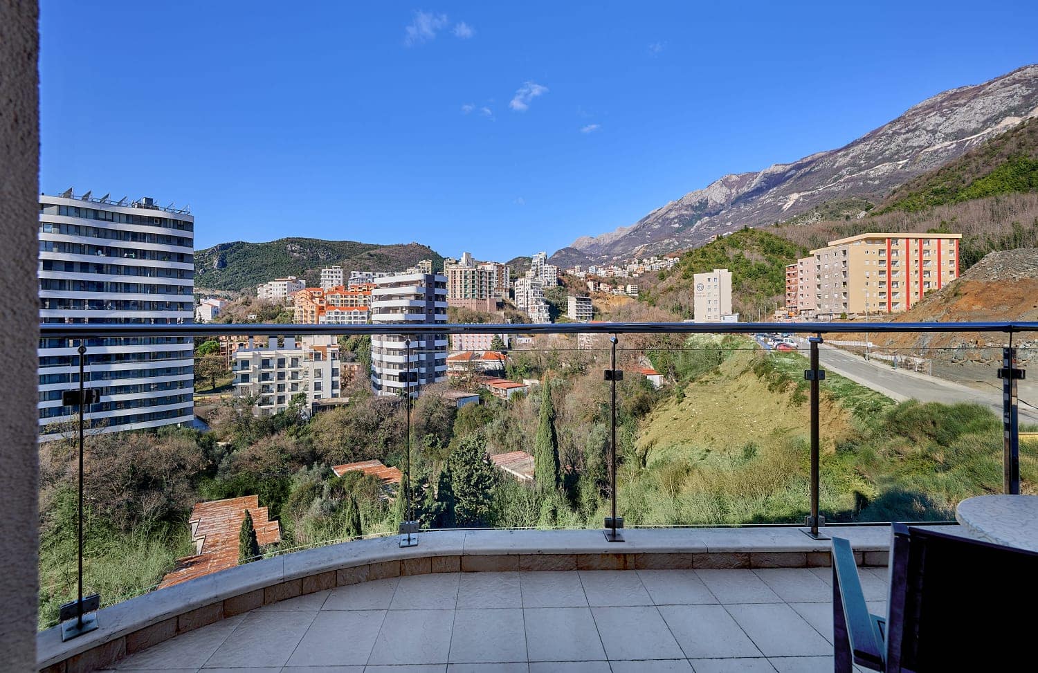 Pogled sa balkona apartmana u Bečićima, Crna Gora: panorama planina, moderne gradnje i zelenih brda po sunčanom danu.