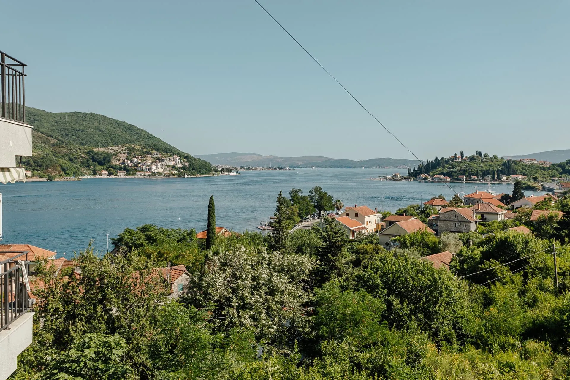 Vue panoramique depuis le balcon de l’appartement à Kamenari, Monténégro : baie de Kotor, montagnes, verdure et toits en tuiles des maisons.