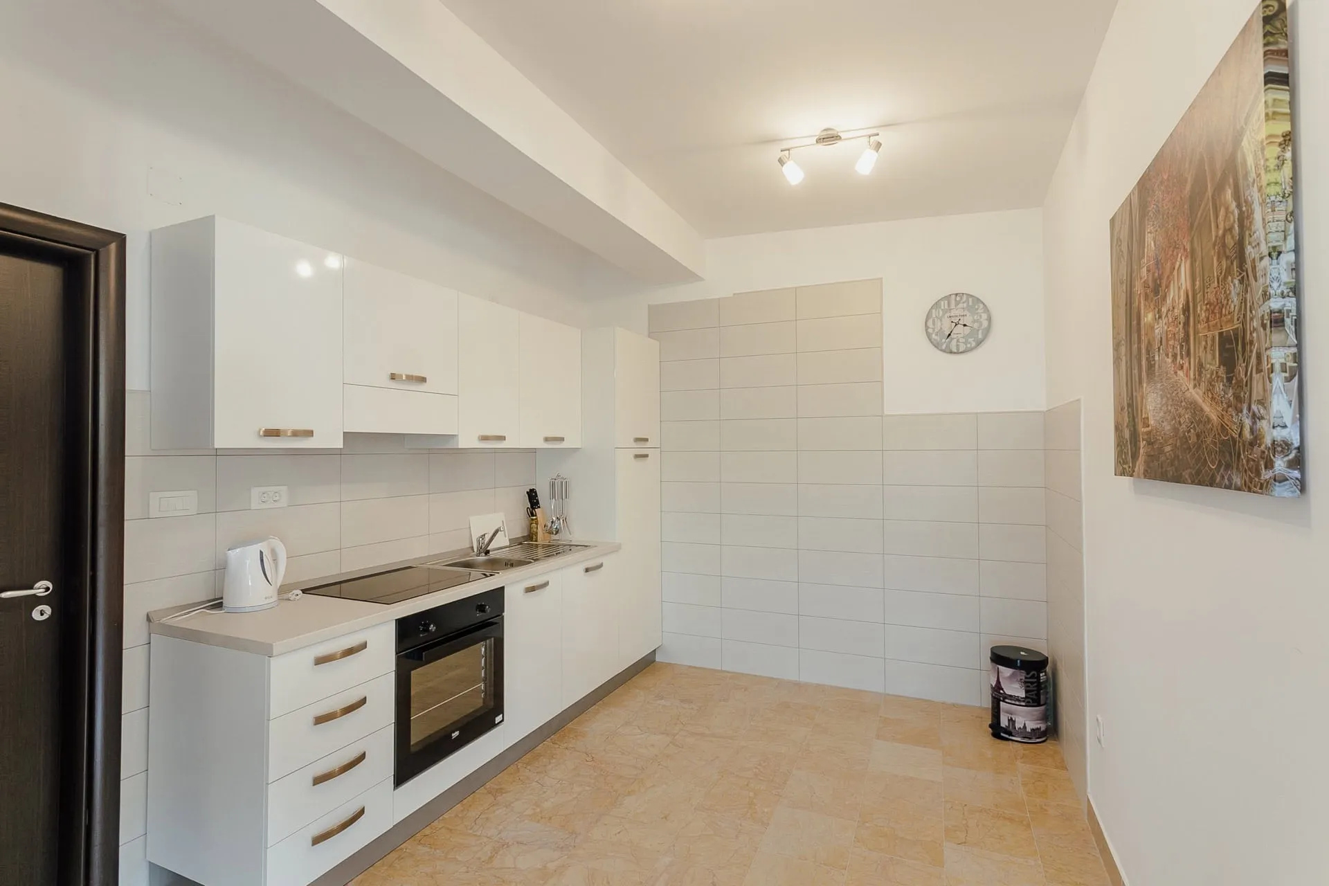 Cuisine blanche moderne dans un appartement à Kamenari, Monténégro : électroménager intégré, carrelage au sol et intérieur lumineux.