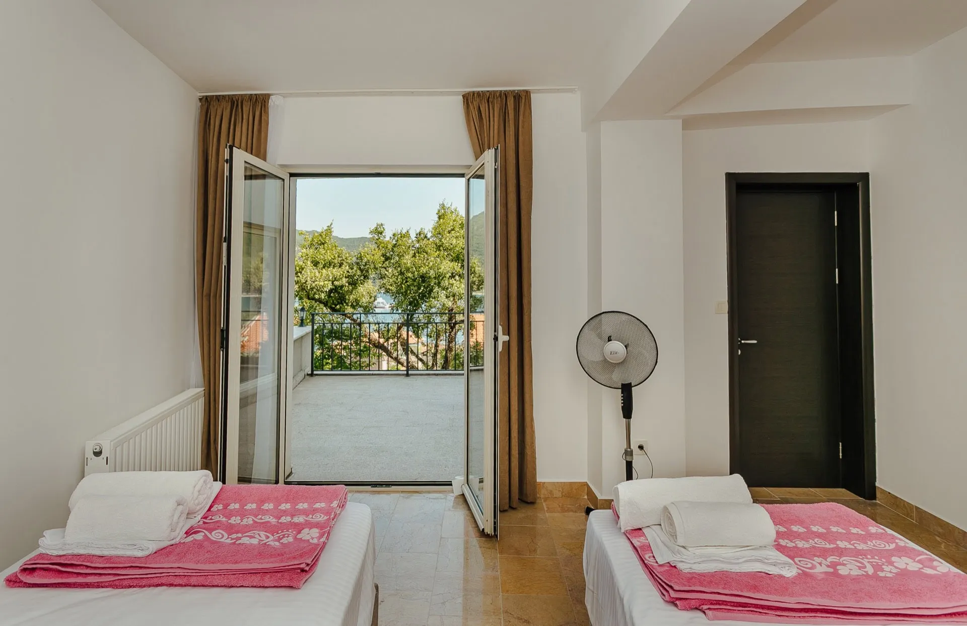 Chambre dans un appartement à Kamenari, Monténégro : deux lits, accès à la terrasse avec vue sur la mer et les montagnes, intérieur lumineux.
